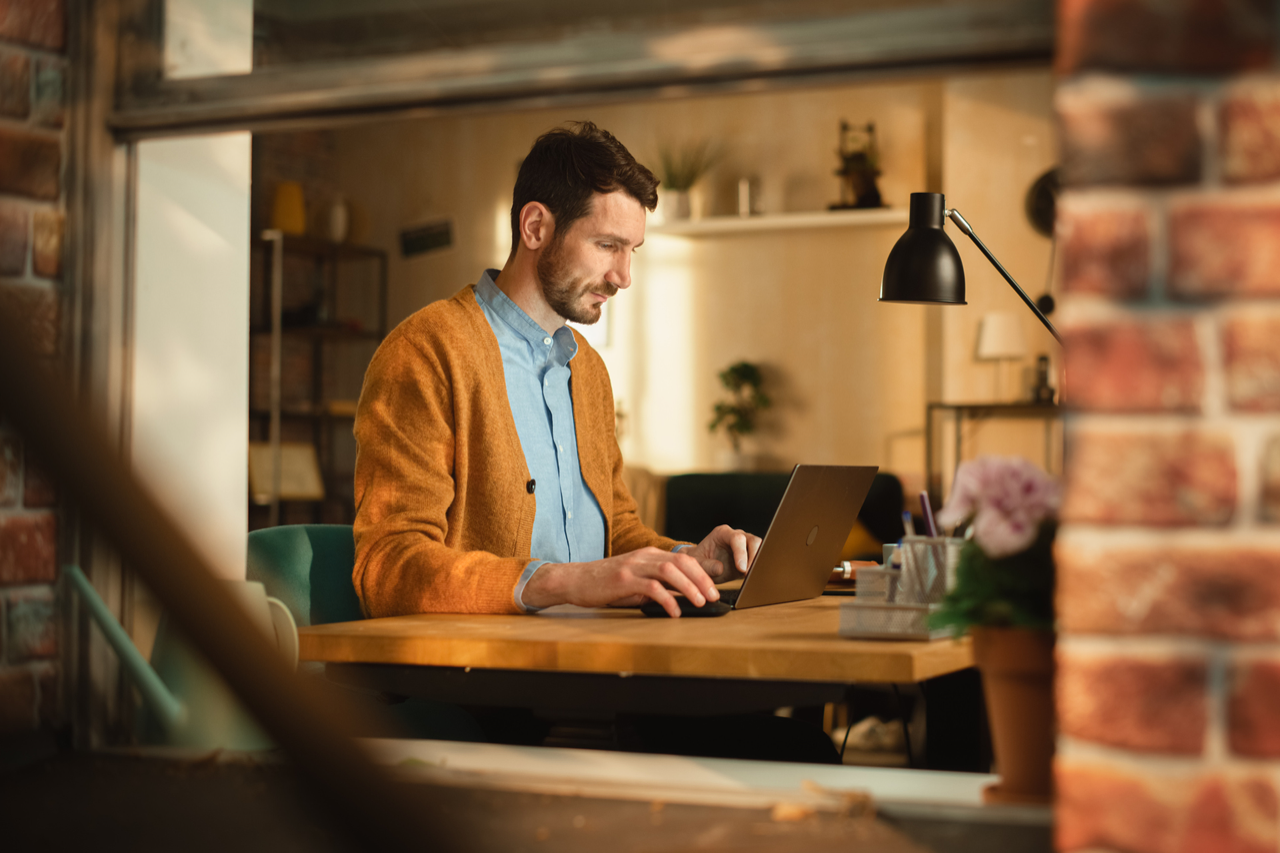 Man working on a laptop at a desk in a cozy home office.